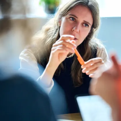 Copywriter Trees heeft oranje stylo vast en luistert naar de gespreksleider van de meeting