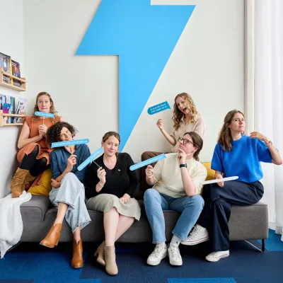 Bliksem Schrijfbureau poseert zittend in de zetel voor het logo, met een tekstballon in de hand