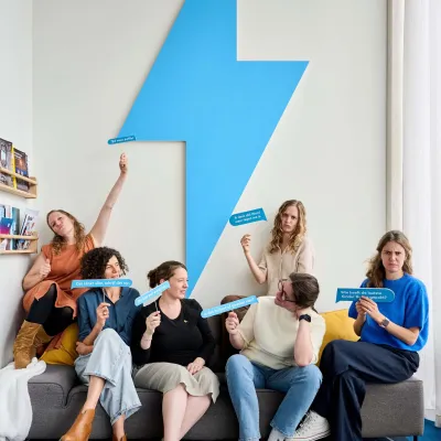 Bliksem Schrijfbureau zit samen in de zetel en iedereen van het team houdt een tekstballon in de lucht