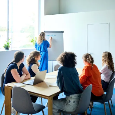 Het team van Bliksem Schrijfbureau zit aan de vergadertafel en kijkt naar Marlies die notities neemt op het whiteboard