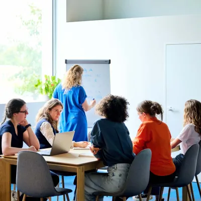 5 copywriters van Bliksem Schrijfbureau brainstormen aan tafel, terwijl Marlies rechtstaand notities maakt op het bord