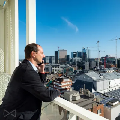 We Invest-makelaar belt met klant vanop het balkon van een gebouw